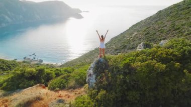Kefalonya 'daki İyon Denizi' ne bakan kayalık bir tepede kollarını kaldıran kadın..
