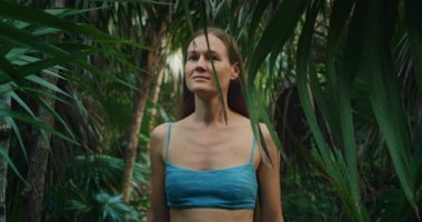 Kadın tropikal yaprakların arasında yürür ve sakin bir şekilde orman palmiyesi ormanına bakar..