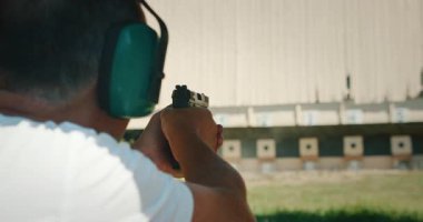 Atış menzilinde mermi kovanı fırlatılırken, adam kulaklık takan hedeflere tabanca ateşliyor..
