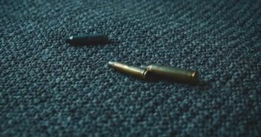 Mermi kovanları dökülüp atış poligonundaki desenli halı döşemesine saçılmış..