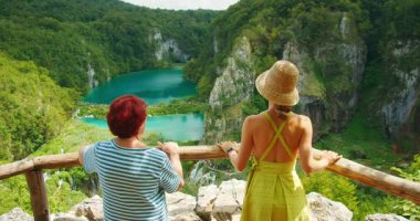 Yaz boyunca Plitvice Gölleri Ulusal Parkı 'ndaki turkuaz göller ve uçurumların panoramik manzarasının keyfini çıkaran iki kadın.