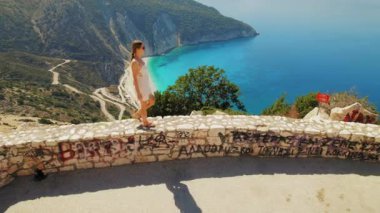 Güneşli bir yaz gününde Kefalonia 'daki Myrtos Plajı' na bakan duvarda yürüyen bir turist..