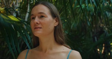 Yoğun orman ışığında etrafı tropikal bitkilerle çevrili bir kadın..