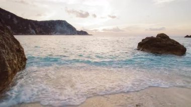 Yaz deniz dalgaları gün batımında sakin bir çakıl taşlı plajda yavaşça kıyıya vurur..