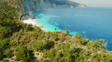 Kefalonya 'daki çarpıcı beyaz çakıl taşı plajının üzerindeki bir uçurumda kutlama yapan kadın Yunanistan.