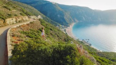 Beyaz elbiseli kadın, Yunanistan 'ın Kefalonia adasındaki Petani Sahili' nin geniş manzarasına hayran..