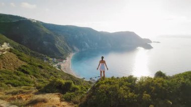 Kefalonia 'nın yüksek uçurum kenarından sabah güneşinde geniş sahil koyuna bakan bir kadın..