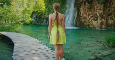Ahşap köprüde duran kadın doğa parkındaki şelaleye bakıyor..