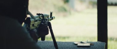 Adam açık alanda atış talimi sırasında uzak mesafeden hedef alan bipoda tüfekle yatıyor ve ateş ediyor..