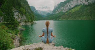 Dağlarla çevrili zümrüt yeşili Gosau gölünde meditasyon yapan bir kadın..