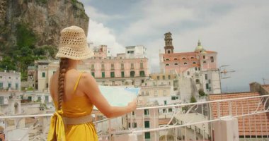 Turist kadın İtalya kıyılarındaki güneşli bir Atrani kasabasını keşfederken haritaya bakıyor..