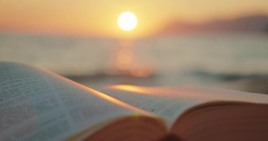 Sıcak yaz akşamlarında gün batımıyla aydınlanan bir sahilde açık bir kitap..