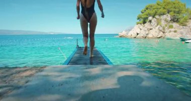 Mayo giymiş bir kadın güneşli yaz gününde açık turkuaz denize atlıyor..