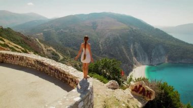 Kefalonya 'da yaz aylarında plajın üstündeki dağ manzarasına bayılan kadın görülüyor.