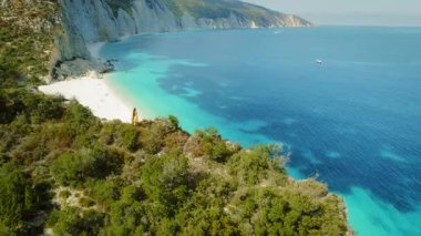 Yazın Kefalonia Yunanistan 'da, turkuaz plaj kayalıklarının üzerinde giyinmiş bir kadın duruyor.