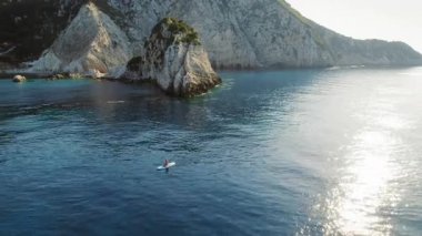 Kefalonia 'daki kayalık bir adanın kıyısındaki mavi sularda kürek çeken kişi..