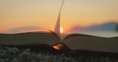 Hırvatistan 'da yaz aylarında çakıllı bir plajda gün batımında rüzgarda savrulan bir kitabın sayfası..