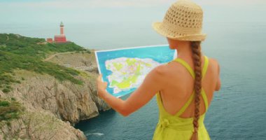 Kadın, İtalya Capri 'de deniz feneri Punta Carena manzaralı harita eğitimi alıyor..