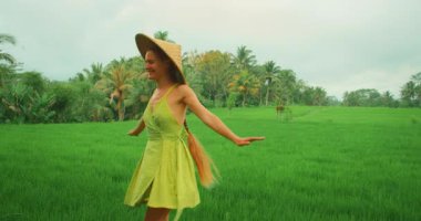 Bali 'de bulutlu gökyüzünün altında açık yeşil pirinç tarlasında dans eden mutlu kadın..