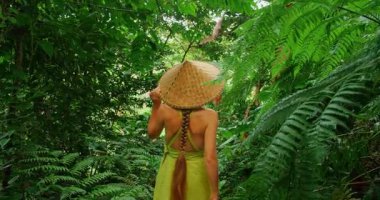 Bali 'de yoğun tropikal ormanda konik şapkalı bir kadın turist yürüyor..