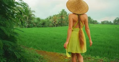 Bali 'de yaz mevsiminde yemyeşil pirinç tarlasında yürüyen bir kadın.