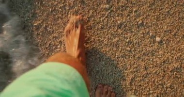 Hırvatistan 'ın yaz aylarında gün batımında ıslak çakıllı sahil şeridinde yalınayak yürüyen bir adam.