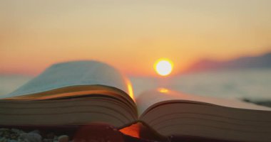 An open book on a beach at sunset with a calm sea in summer.