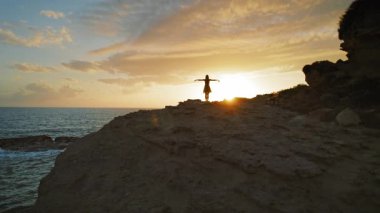 Kefalonya 'nın Kefalonya kıyılarında gün batımında kollarını kaldırmış uçurumdaki kadın silueti.
