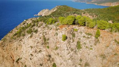 Kefalonya kıyılarında mavi denizin üzerinde çam ağaçları olan kayalık kayalıklarda koşan bir kadın..