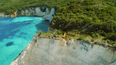 Kefalonya 'nın turkuaz körfezinin üzerindeki uçurumda kollarını kaldırmış dans eden kadın Yunanistan.