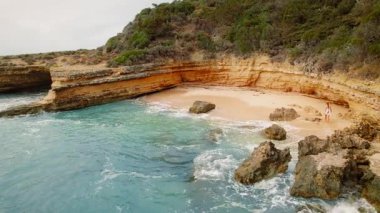 Etrafı kayalıklarla çevrili tenha kumlu bir koy ve beyaz elbiseli bir kadın yürüyor..