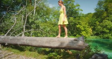 Genç kadın yazın bereketli Plitvice Gölleri ormanında ağaç gövdesinde çıplak ayakla yürüyor..