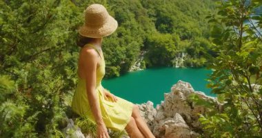 Hırvatistan 'da yaz aylarında Plitvice Gölleri Ulusal Parkı' nın manzarasına hayran olan genç bir kadın uçurumun kenarında oturuyor.