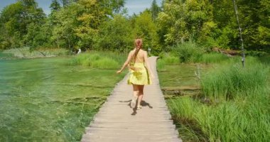Yazın Plitvice 'de temiz göl üzerinden tahta yoldan geçen bir kadın..