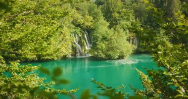 Hırvatistan 'da yoğun yeşil yapraklardan sakin turkuaz göle şelale yükseliyor.