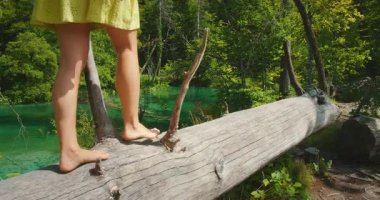 Çıplak ayaklı kadın, Plitvice Gölleri Ulusal Parkı 'ndaki turkuaz suyun üzerinde bir kütük üzerinde dengede duruyor..