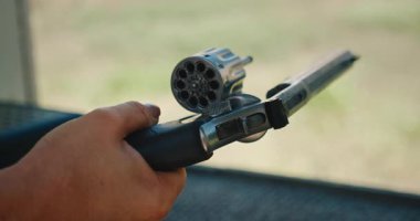 Elinde silah tutan kişi mermiler için çoklu boş silindir odalarını gösteriyor..