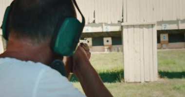 Güneşli bir poligondaki hedeflere nişan alıp ateş eden bir adam..