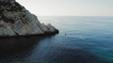 Kefalonya 'nın sakin mavi sularında kayalıkların yanında kürek çeken insanlar..
