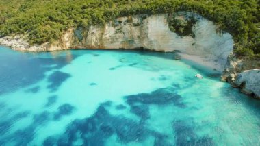 Yunanistan 'da yemyeşil ormanı ve yüksek uçurumları olan beyaz bir kumsal yakınında demirlemiş bir tekne..
