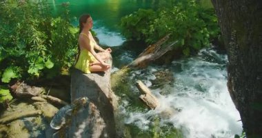 Huzurlu orman ortamında zümrüt deresinin yanında meditasyon yapan bir kadın..