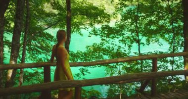 Plitvice Ulusal Parkı 'ndaki zümrüt gölünün yanındaki ağaçların gölgesinde, tahta yolda yürüyen kadın..