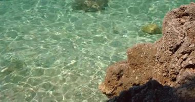 Yaz aylarında kayalık kıyıların yanındaki saydam sığ denizde yansıyan güneş ışığı..
