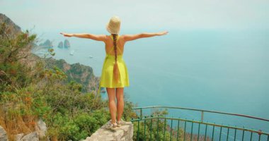 Yazın Capri 'den gelen Faraglioni deniz yığınlarıyla kıyı manzarasının tadını çıkaran kadın..