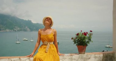 Güneşli yaz gününde Atrani şehrinde denize bakan duvarda dinlenen bir kadın..