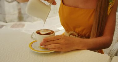 İtalyan kasabasındaki kafe masasında bir kadının espresso 'ya süt dökmesi..