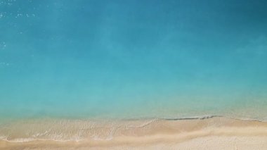 Turkuaz suyla kıyı şeridinin havadan görünüşü yavaşça kumlu kumsalla buluşuyor..