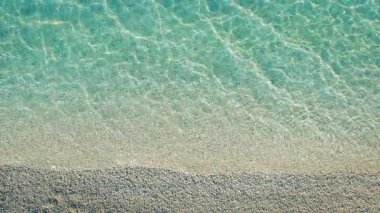 Kristal berraklığında sığ suların detaylı hava manzarası yazın Yunanistan 'da Kefalonya' da el değmemiş beyaz çakıllı bir sahili nazikçe süpürüyor.