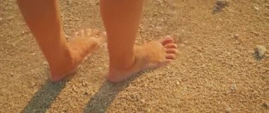 Kaba kumlu plajda çıplak ayakla ayakta duran bir çocuk ve sıcak güneş ışığı..