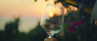 Gün batımında açık havada beyaz şarap bardağa dökülüyor..